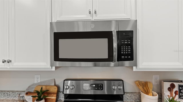 room details featuring stainless steel appliances, white cabinetry, and light stone countertops