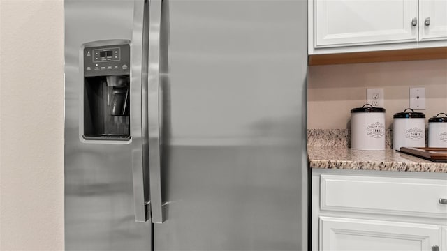 details with stainless steel refrigerator with ice dispenser, light stone counters, and white cabinets