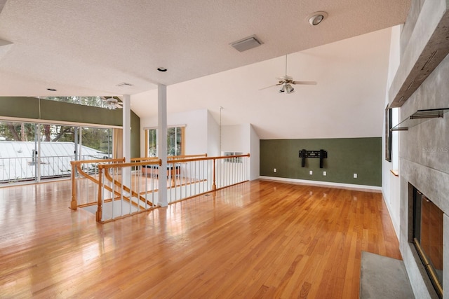 unfurnished living room featuring a textured ceiling, a fireplace, light hardwood / wood-style floors, vaulted ceiling, and ceiling fan