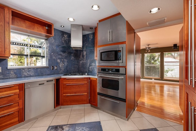 kitchen with light tile patterned flooring, appliances with stainless steel finishes, island range hood, and tasteful backsplash