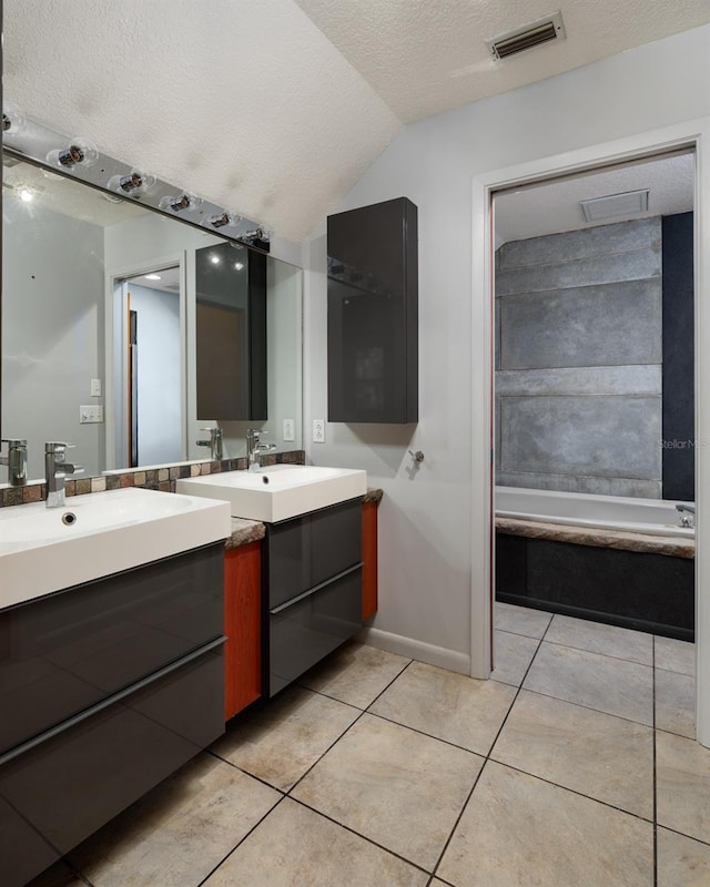 bathroom featuring vaulted ceiling, a bathtub, tile patterned floors, a textured ceiling, and vanity