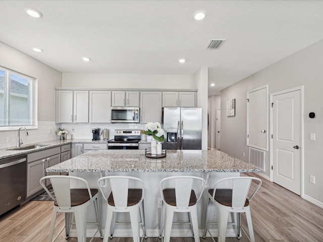 kitchen with appliances with stainless steel finishes, sink, light stone counters, and a center island