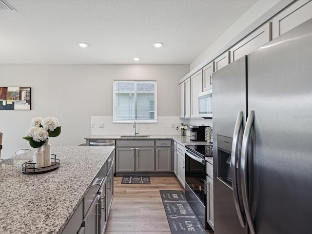 kitchen featuring stainless steel appliances, gray cabinetry, backsplash, light hardwood / wood-style flooring, and sink