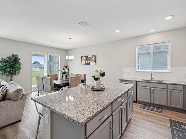 kitchen with light hardwood / wood-style floors, decorative backsplash, hanging light fixtures, a kitchen island, and sink