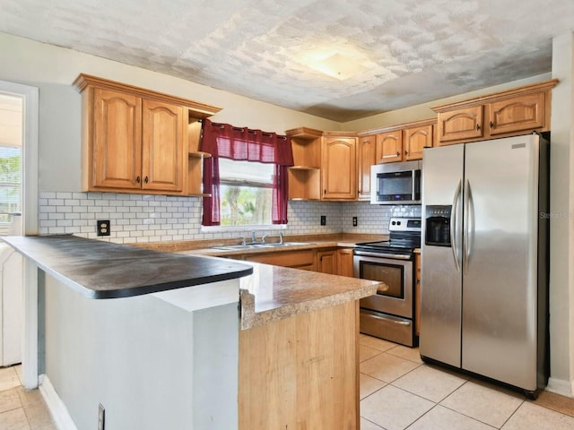 kitchen with backsplash, kitchen peninsula, sink, appliances with stainless steel finishes, and light tile patterned floors