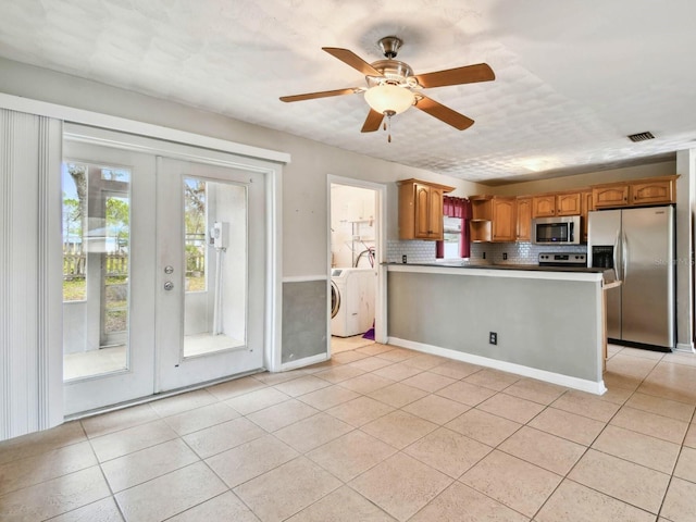 kitchen featuring appliances with stainless steel finishes, washer / clothes dryer, french doors, tasteful backsplash, and light tile patterned floors