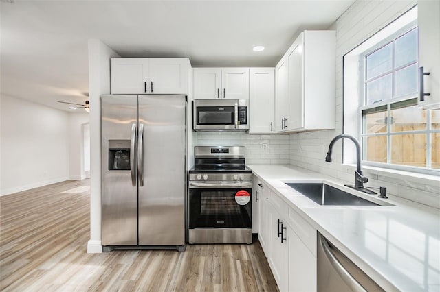 kitchen with sink, light wood-type flooring, white cabinets, and appliances with stainless steel finishes