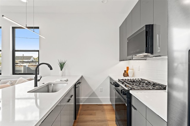 kitchen with hardwood / wood-style floors, gray cabinets, decorative backsplash, black appliances, and sink