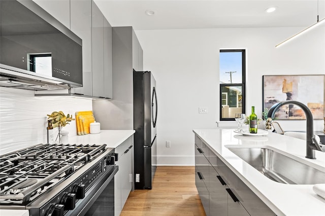 kitchen featuring appliances with stainless steel finishes, gray cabinetry, tasteful backsplash, light hardwood / wood-style flooring, and sink