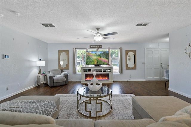 living room featuring dark wood-type flooring, ceiling fan, and a textured ceiling