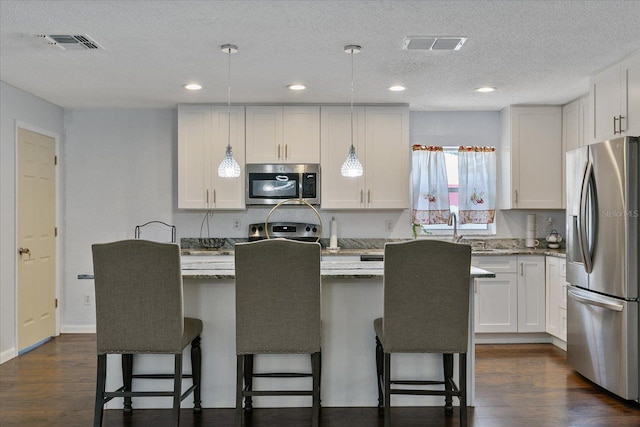 kitchen featuring hanging light fixtures, appliances with stainless steel finishes, white cabinets, and light stone counters