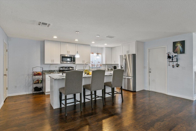 kitchen with dark wood-type flooring, hanging light fixtures, a kitchen island, stainless steel appliances, and white cabinets