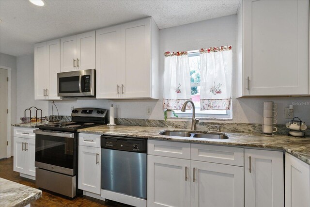 kitchen with appliances with stainless steel finishes, sink, white cabinets, light stone countertops, and a textured ceiling