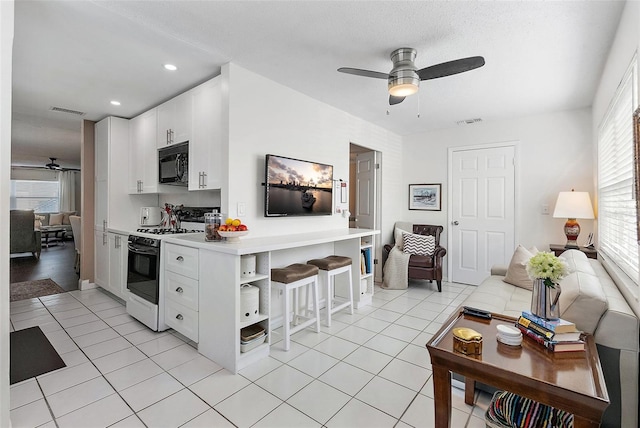 kitchen featuring a kitchen breakfast bar, ceiling fan, white cabinets, white gas range oven, and light tile patterned flooring