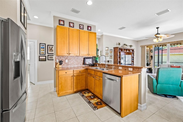 kitchen featuring appliances with stainless steel finishes, sink, ornamental molding, light tile patterned floors, and kitchen peninsula