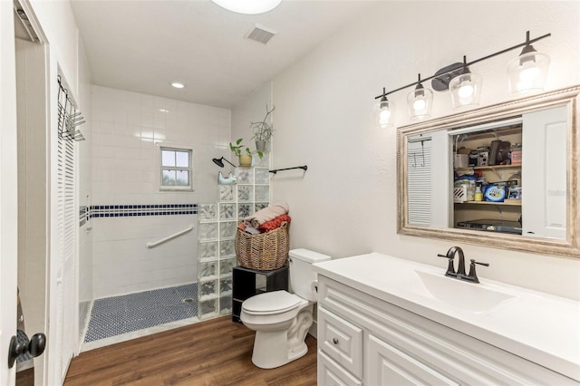 bathroom with hardwood / wood-style flooring, tiled shower, vanity, and toilet