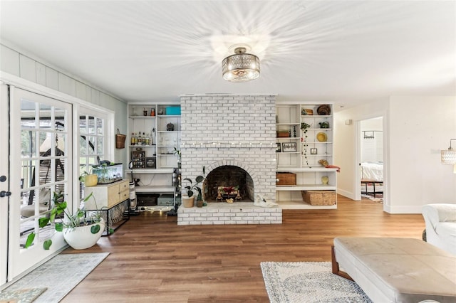 living area featuring built in shelves, a brick fireplace, baseboards, and wood finished floors