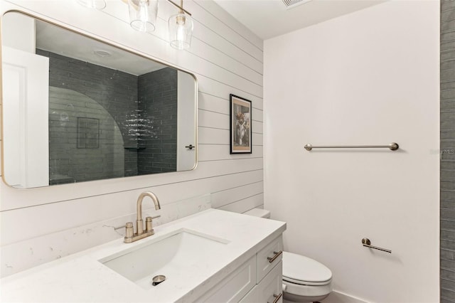 full bath with toilet, a tile shower, wood walls, and vanity