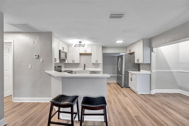 kitchen featuring appliances with stainless steel finishes, white cabinetry, sink, light wood-type flooring, and a breakfast bar area