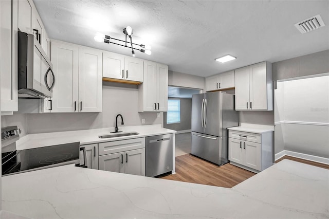 kitchen featuring sink, light wood-type flooring, light stone countertops, stainless steel appliances, and white cabinets