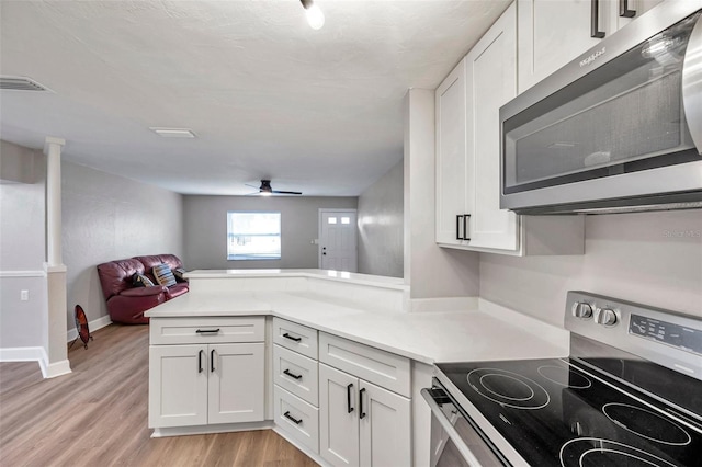 kitchen with white cabinets, stainless steel appliances, kitchen peninsula, ceiling fan, and light hardwood / wood-style flooring