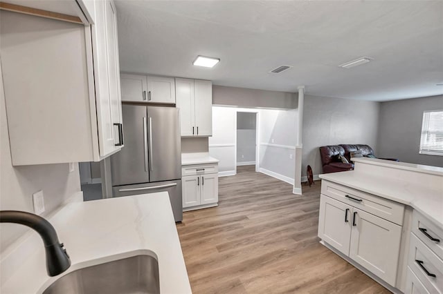 kitchen with light hardwood / wood-style floors, white cabinets, stainless steel fridge, and sink