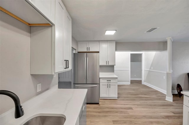 kitchen featuring light stone countertops, white cabinetry, sink, stainless steel refrigerator, and light hardwood / wood-style flooring