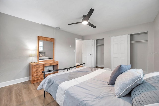 bedroom with ceiling fan, two closets, and hardwood / wood-style flooring