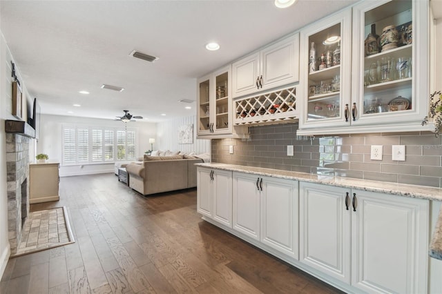 kitchen with a stone fireplace, white cabinets, dark hardwood / wood-style flooring, ceiling fan, and light stone counters