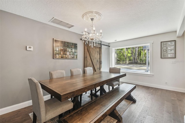 dining space featuring a notable chandelier, dark wood-type flooring, a barn door, and a textured ceiling