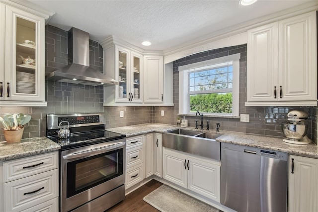 kitchen featuring stainless steel appliances, white cabinetry, and wall chimney range hood