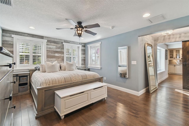 bedroom with a textured ceiling, dark wood-type flooring, ceiling fan, and wood walls