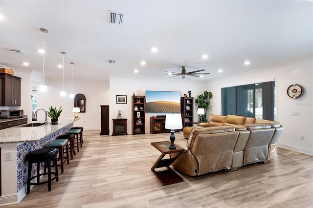 living room featuring ceiling fan, sink, ornamental molding, and light wood-type flooring