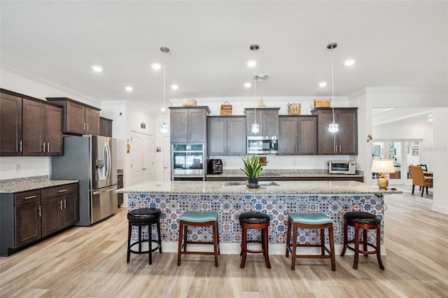 kitchen with dark brown cabinets, decorative light fixtures, a kitchen bar, a kitchen island with sink, and stainless steel appliances