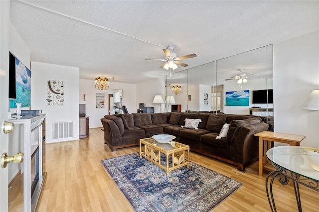 living room featuring hardwood / wood-style flooring, ceiling fan with notable chandelier, and a textured ceiling