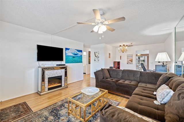 living room featuring ceiling fan with notable chandelier, a fireplace, a textured ceiling, and light hardwood / wood-style flooring