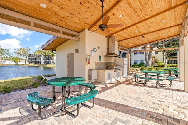 view of patio with a water view, ceiling fan, and exterior kitchen