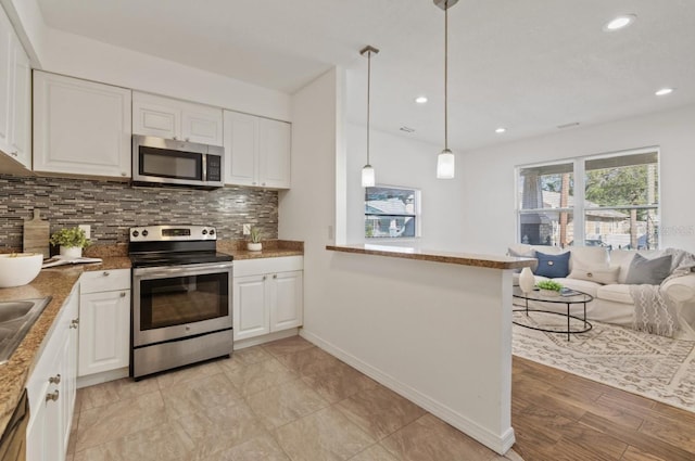 kitchen with kitchen peninsula, appliances with stainless steel finishes, white cabinetry, and decorative light fixtures