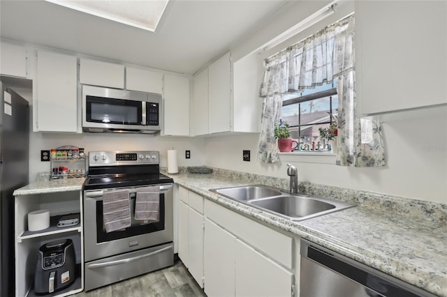 kitchen featuring stainless steel appliances, white cabinetry, sink, and light wood-type flooring