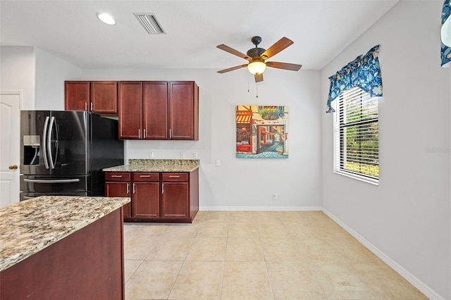 kitchen with light tile patterned floors, stainless steel fridge, light stone countertops, and ceiling fan