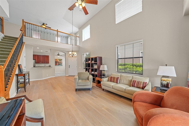 living room with a towering ceiling, light hardwood / wood-style floors, and ceiling fan with notable chandelier