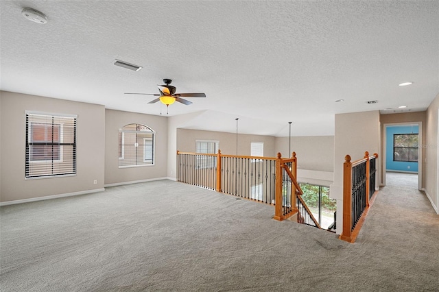 carpeted empty room featuring ceiling fan, a textured ceiling, and a wealth of natural light