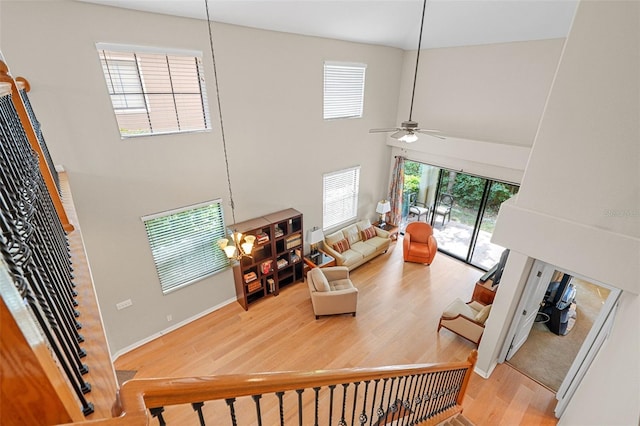 living room featuring hardwood / wood-style floors, ceiling fan with notable chandelier, and a high ceiling