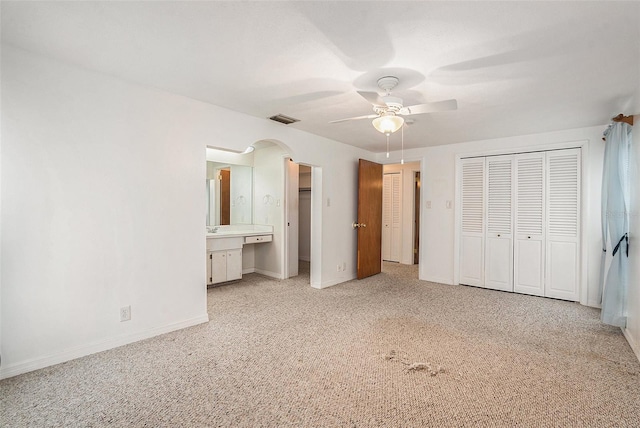 unfurnished bedroom with ceiling fan, light colored carpet, and ensuite bath