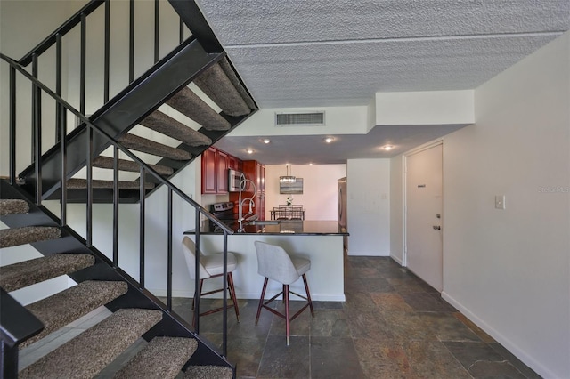 kitchen with appliances with stainless steel finishes, a textured ceiling, a kitchen breakfast bar, and kitchen peninsula