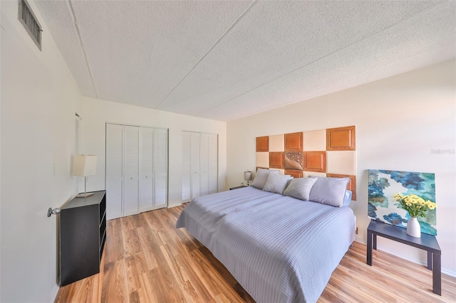 bedroom featuring a textured ceiling, light hardwood / wood-style floors, and multiple closets