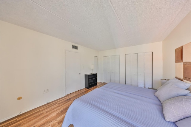 bedroom featuring a textured ceiling, light hardwood / wood-style floors, and multiple closets