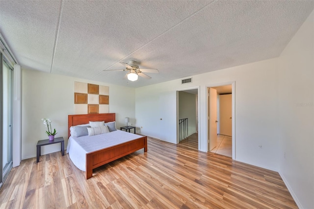 bedroom with ceiling fan, light hardwood / wood-style floors, and a textured ceiling