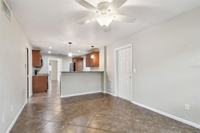 kitchen with kitchen peninsula, ceiling fan, hanging light fixtures, light stone countertops, and stainless steel refrigerator