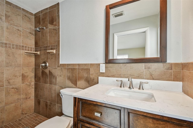 bathroom featuring tile walls, toilet, tiled shower, and vanity